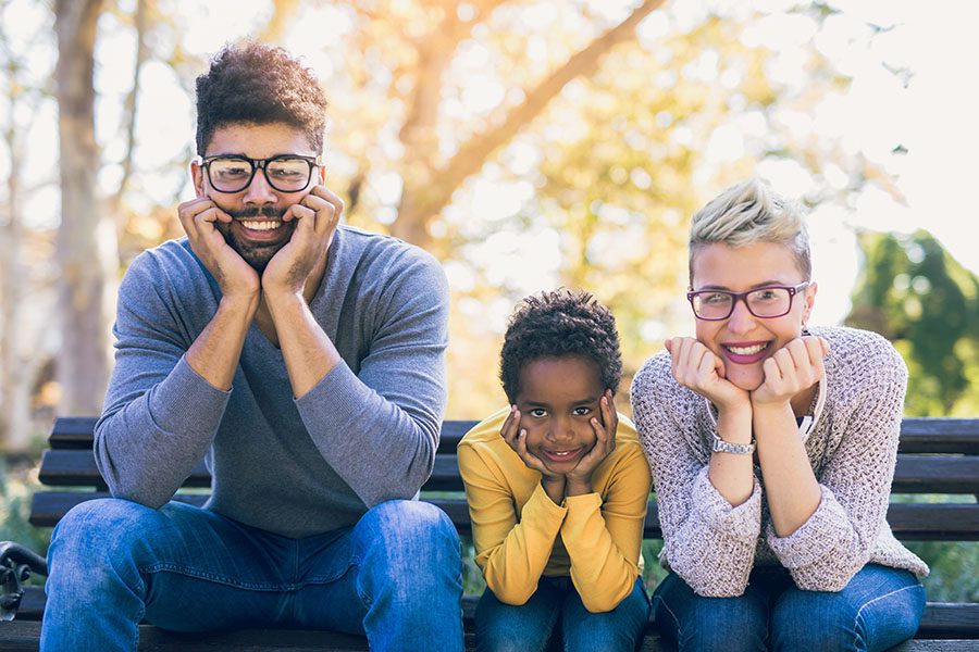 Personal Insurance - Happy Father and Mother With Their Daughter Sit Down at a Bench Resting Their Arms on Their Legs and Holding Their Chins for a Funny Pose